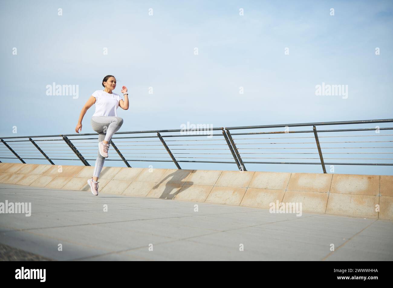 Young woman runner jogger exercising outdoors, running on the city bridge. Female athlete performing morning jog. Determined sportswoman burning calor Stock Photo