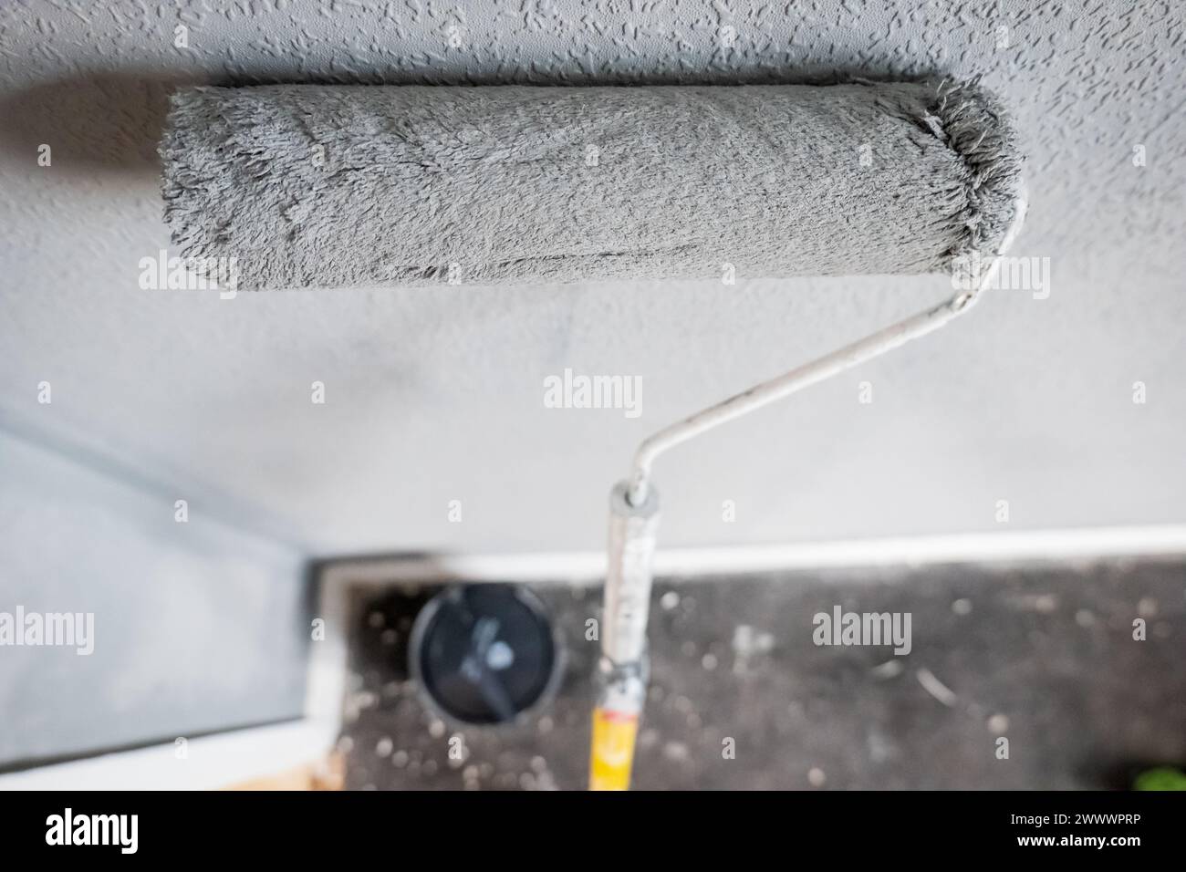Paint roller extendable pole over painted woodchip wallpaper wall