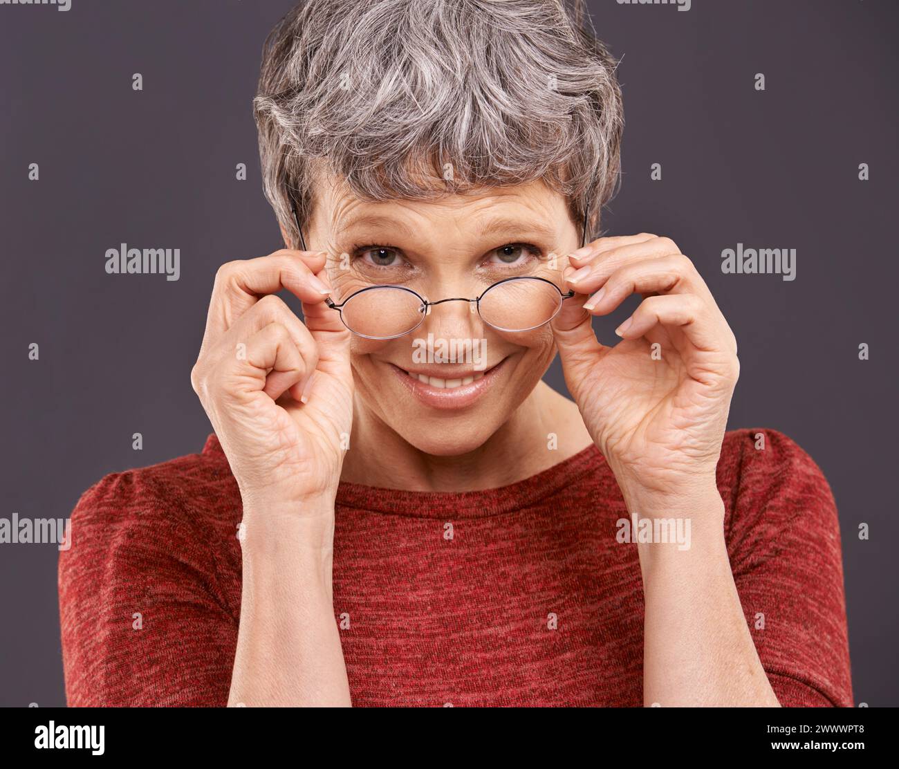 Portrait, senior woman and glasses with smile, retirement and confident pensioner on a grey studio background. Face, old person and elderly lady with Stock Photo