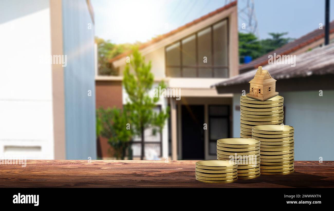 Stack of golden coins and a wooden house on the table with a real ...