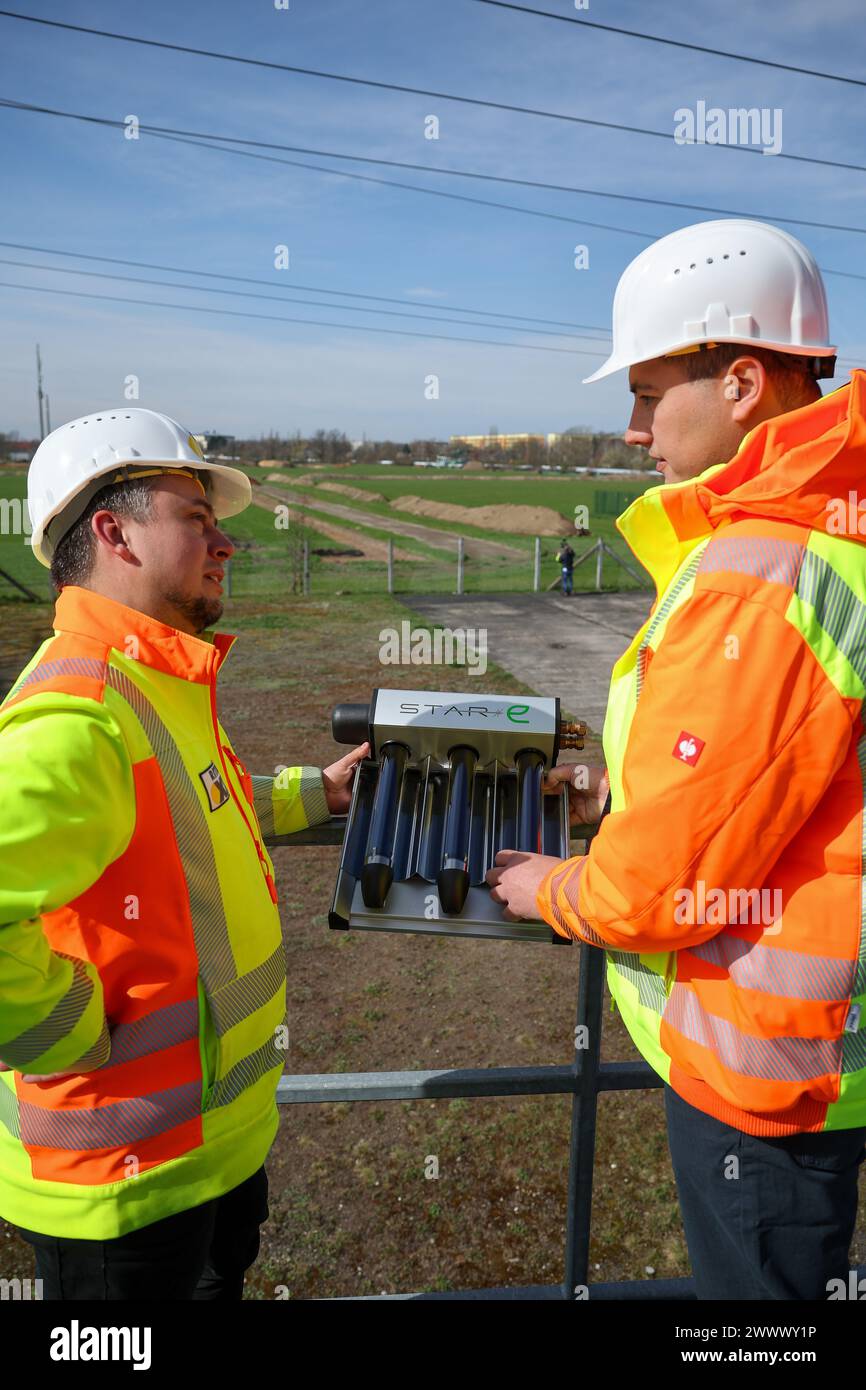 26 March 2024, Saxony, Leipzig: Project managers Guido Wimmer (l) and Paul Gaspar from Ritter Energie stand with a sample of an evacuated tube collector at the construction site for a future solar thermal plant. Over the coming months, a plant consisting of 13,200 solar collectors will be built on the western outskirts of Leipzig. The water, heated to 108 degrees by the sun, will be fed into the city's district heating circuit. This should cover 20 percent of Leipzig's total heating requirements in summer. Stadtwerke is investing 40 million euros in the plant. Heat is to be fed in from 2026. P Stock Photo