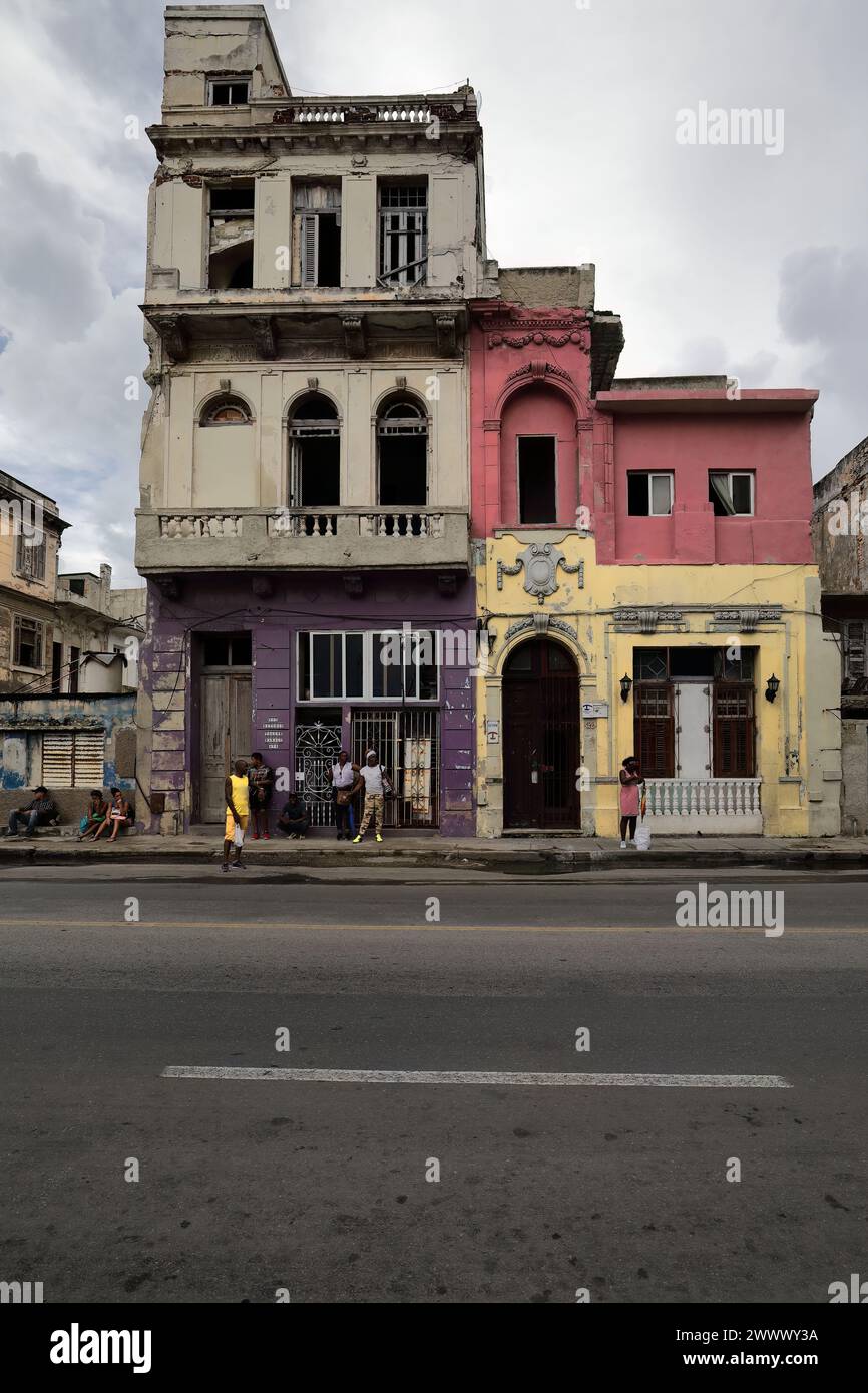 115 Locals at wait for shared taxis, waiting spot on Calle San Lazaro St.sidewalk under colorist facades of stepped, dilapidated houses. Havana-Cuba. Stock Photo