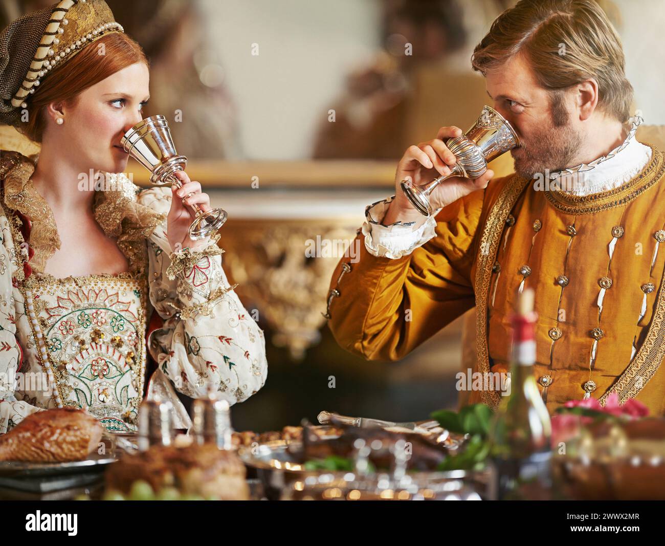 Couple, noble and wine with luxury, feast and renaissance dining table at royal home. King, queen and food with wealth, rich meal and palace or manor Stock Photo