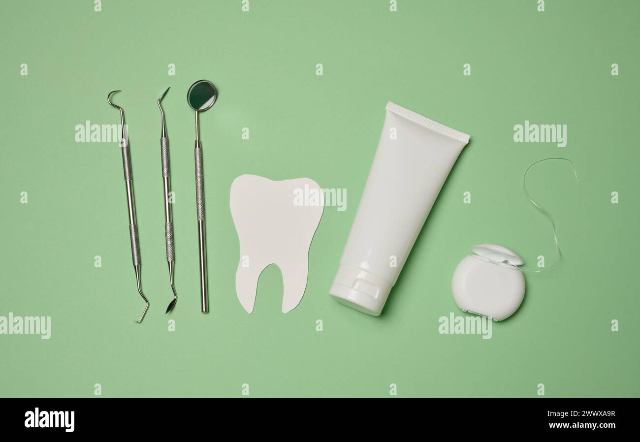 Tube with toothpaste, dental floss and medical mirror on a green ...