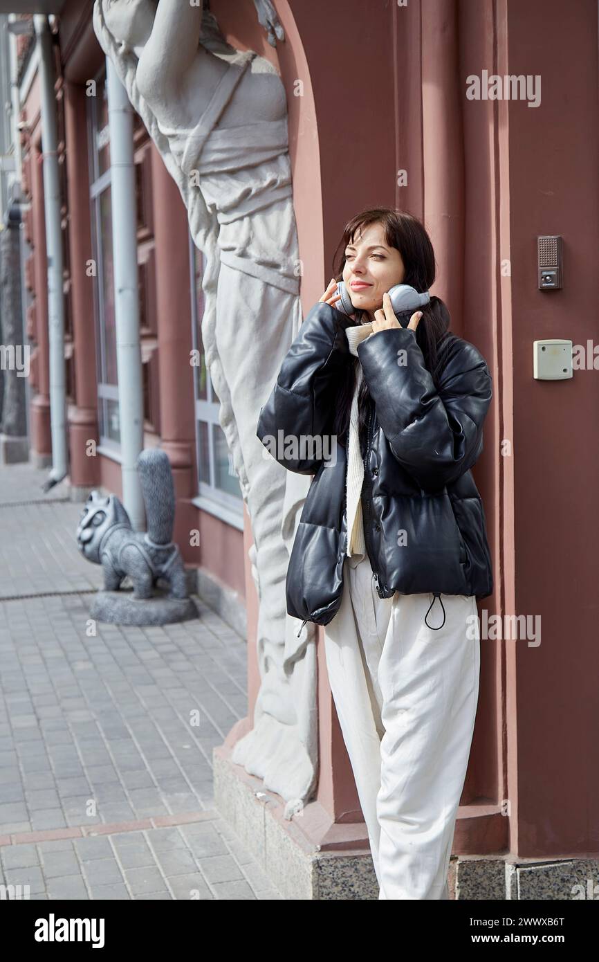 Stylish young woman in earphones listening to music outdoor. Audio healing, learning - taking webinar, casual lifestyle, concept. Stock Photo