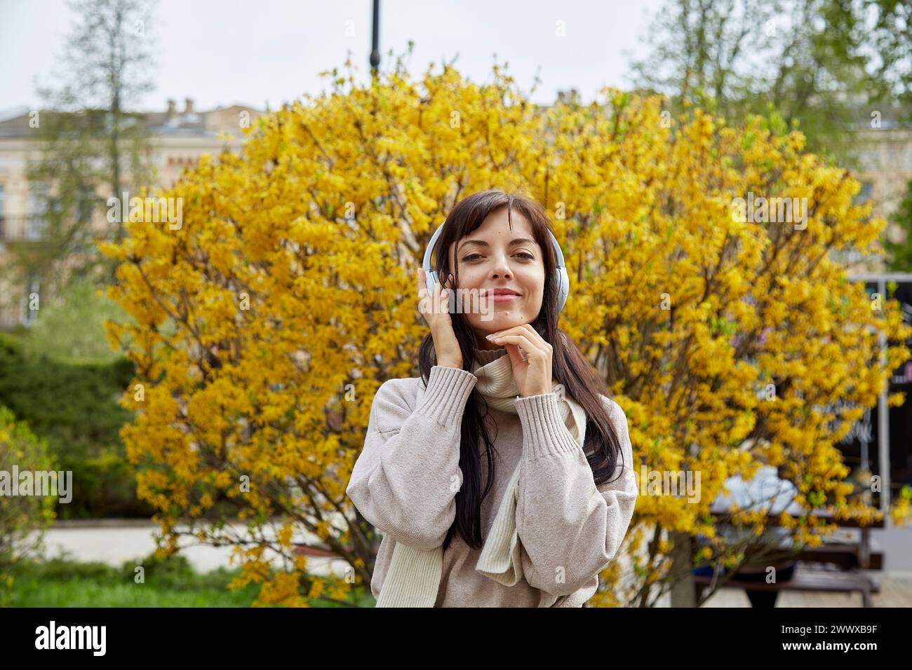 Young woman in earphones listening to music outdoor. Audio healing, learning - taking webinar, casual lifestyle, concept. Stock Photo