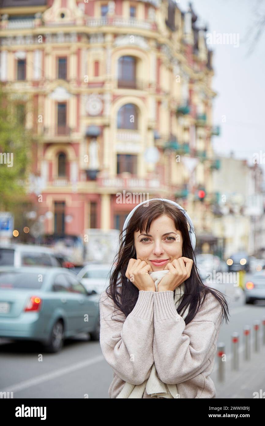 Portrait of young woman in headphones listening to music or taking webinar outdoor. Casual lifestyle, audio healing, learning - concept. Stock Photo
