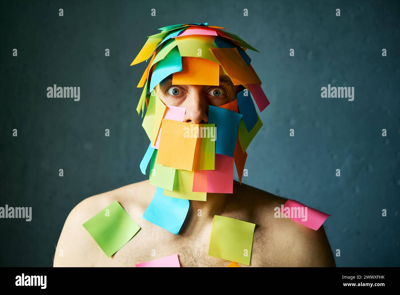 Shocked amazed man with colorful sticky notes all over his face and body over gray background Stock Photo