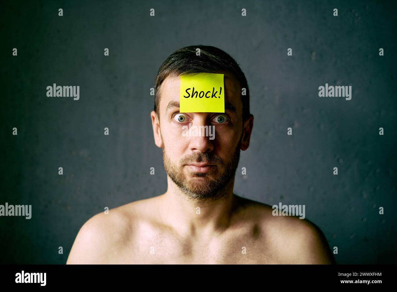 Confused shocked man with yellow sticky note on his forehead over gray background Stock Photo