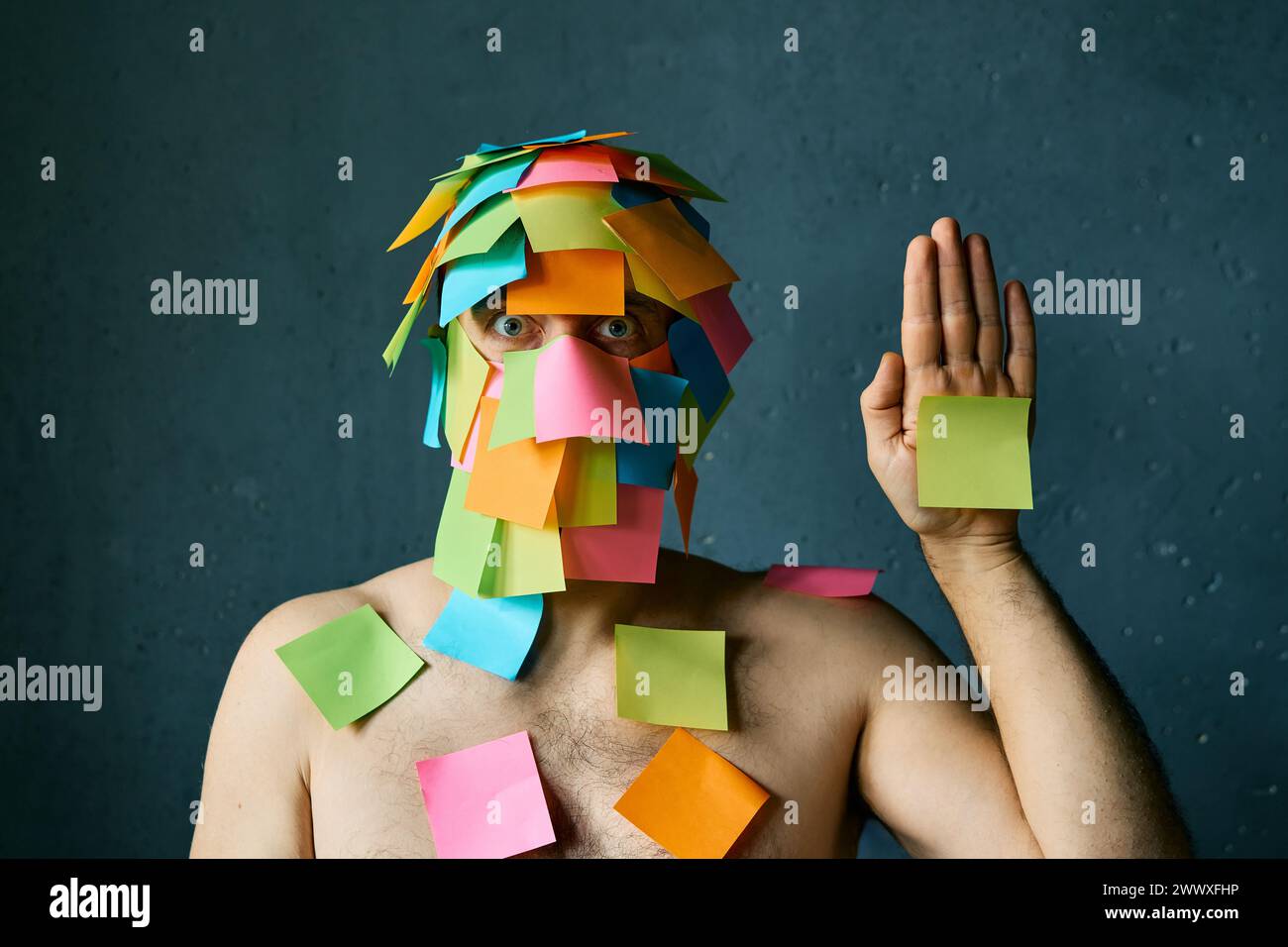 Funny man with colorful sticky notes all over his face and body show palm hand over gray background Stock Photo