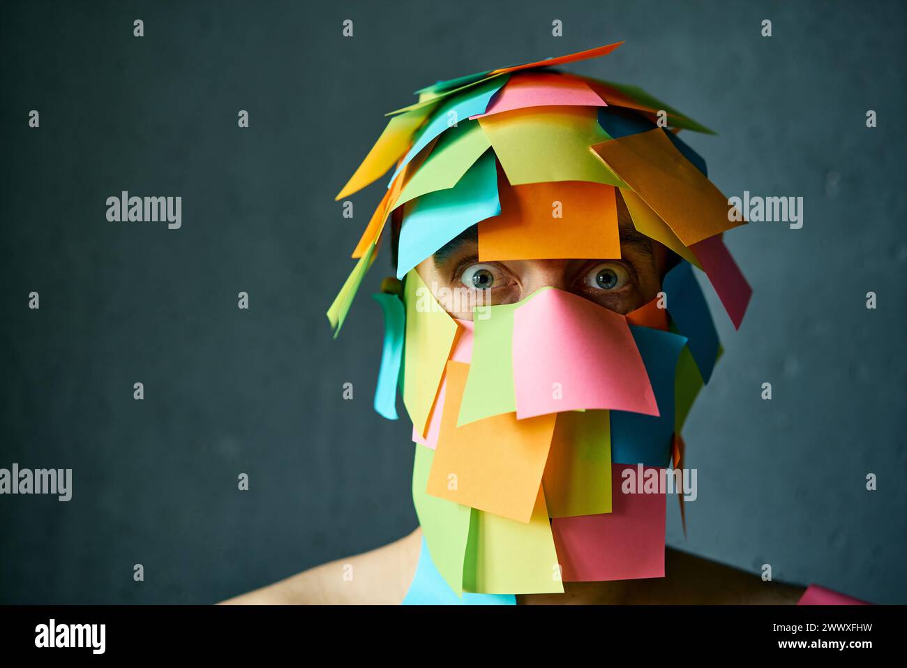Close up portrait of shocked man with colorful sticky notes all over his face over gray background with copy space Stock Photo