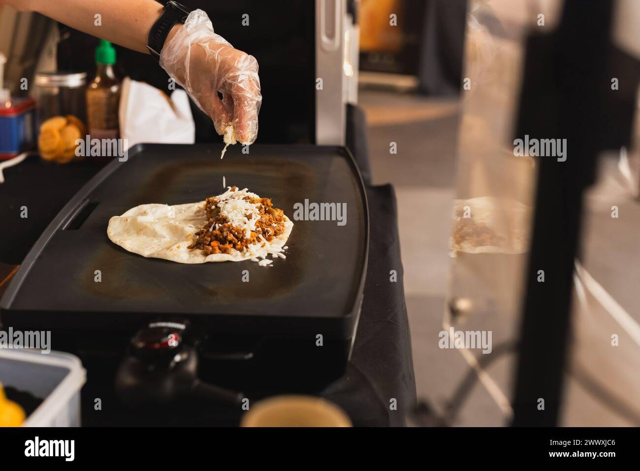 Chef sprinkles a tortilla with cheese preparing fresh quesadilla on ...