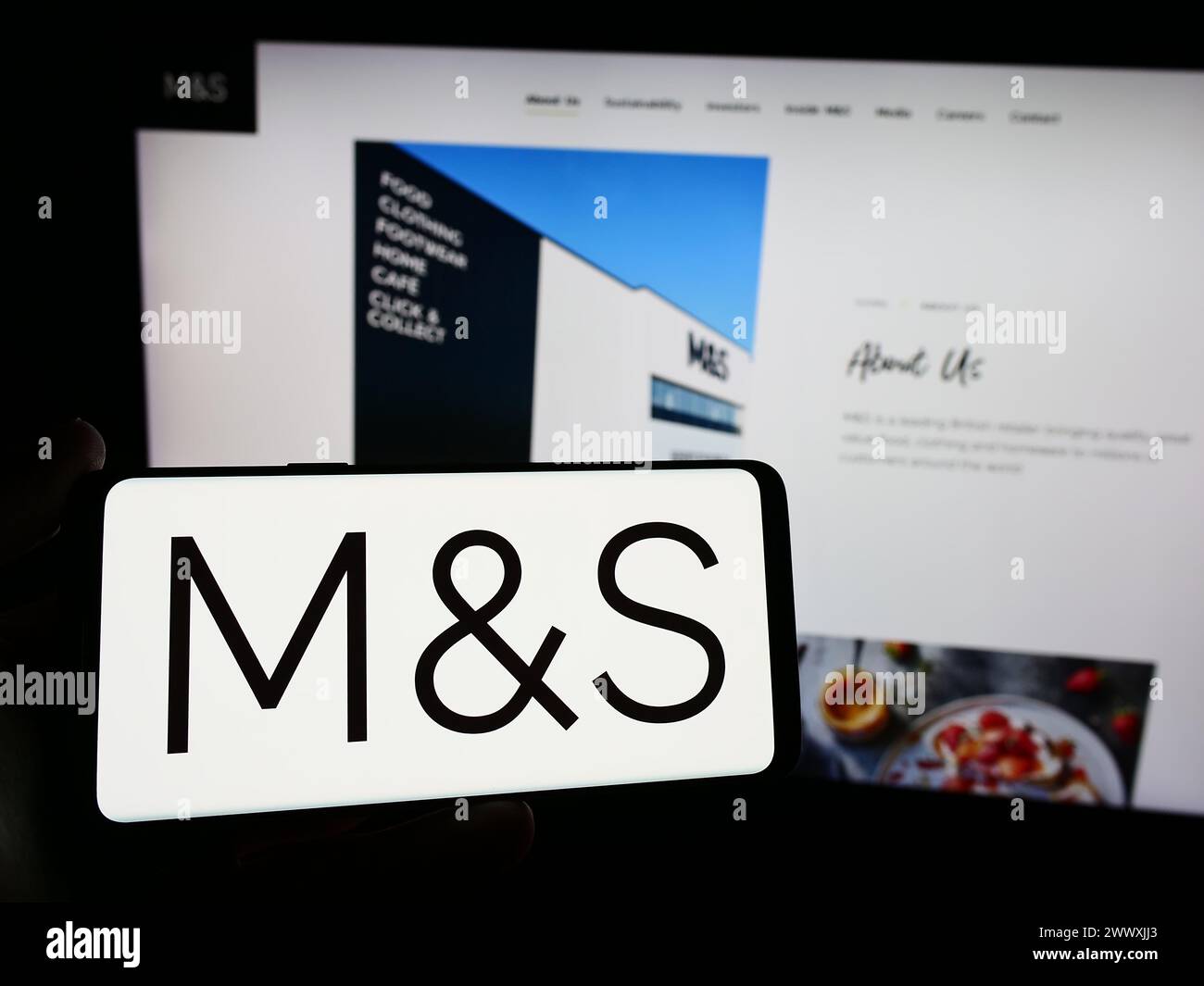 Person holding smartphone with logo of British retail company Marks and Spencer Group plc in front of website. Focus on phone display. Stock Photo