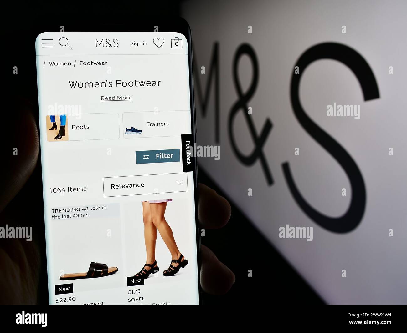 Person holding mobile phone with web page of British retail company Marks and Spencer Group plc with logo. Focus on center of phone display. Stock Photo