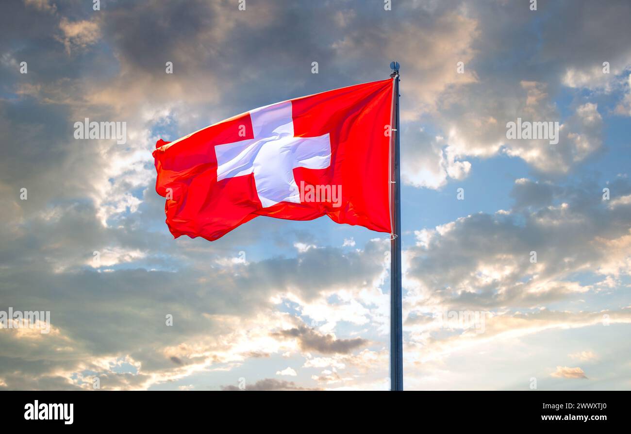 Flag of Switzerland flying in the wind against a cloudy sky. Switzerland national flag waving in the cloudy sky Stock Photo