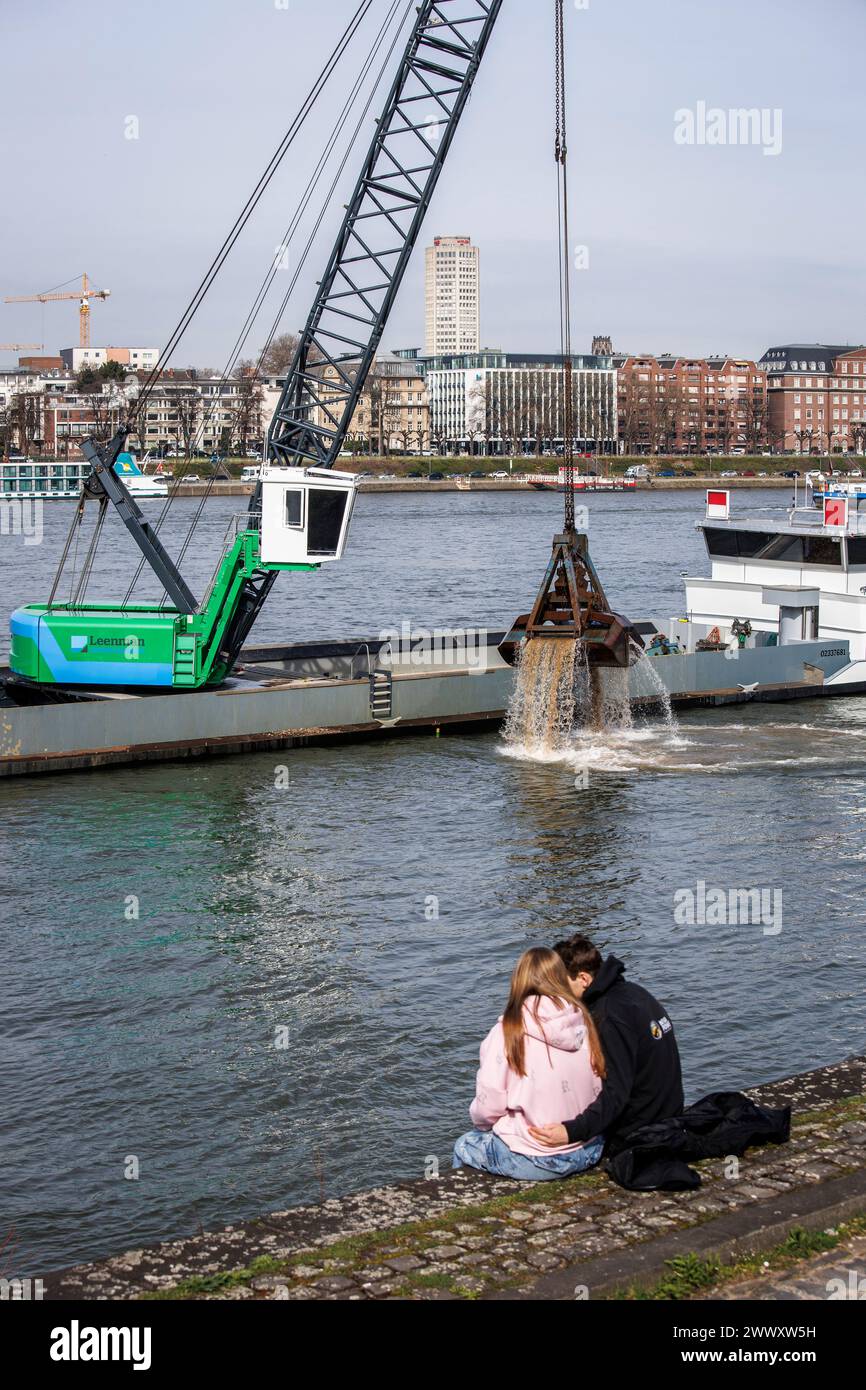 excavator on a ship deepens the riverbed of the river Rhine, couple on the banks in the district Deutz, Cologne, Germany. Bagger auf einem Schiff vert Stock Photo