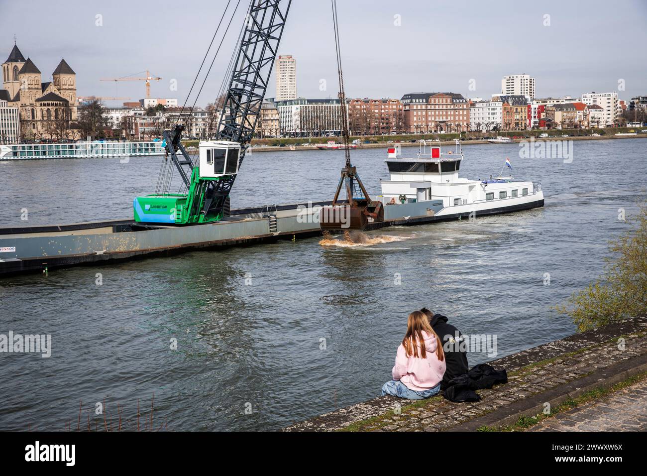excavator on a ship deepens the riverbed of the river Rhine, couple on the banks in the district Deutz, Cologne, Germany. Bagger auf einem Schiff vert Stock Photo