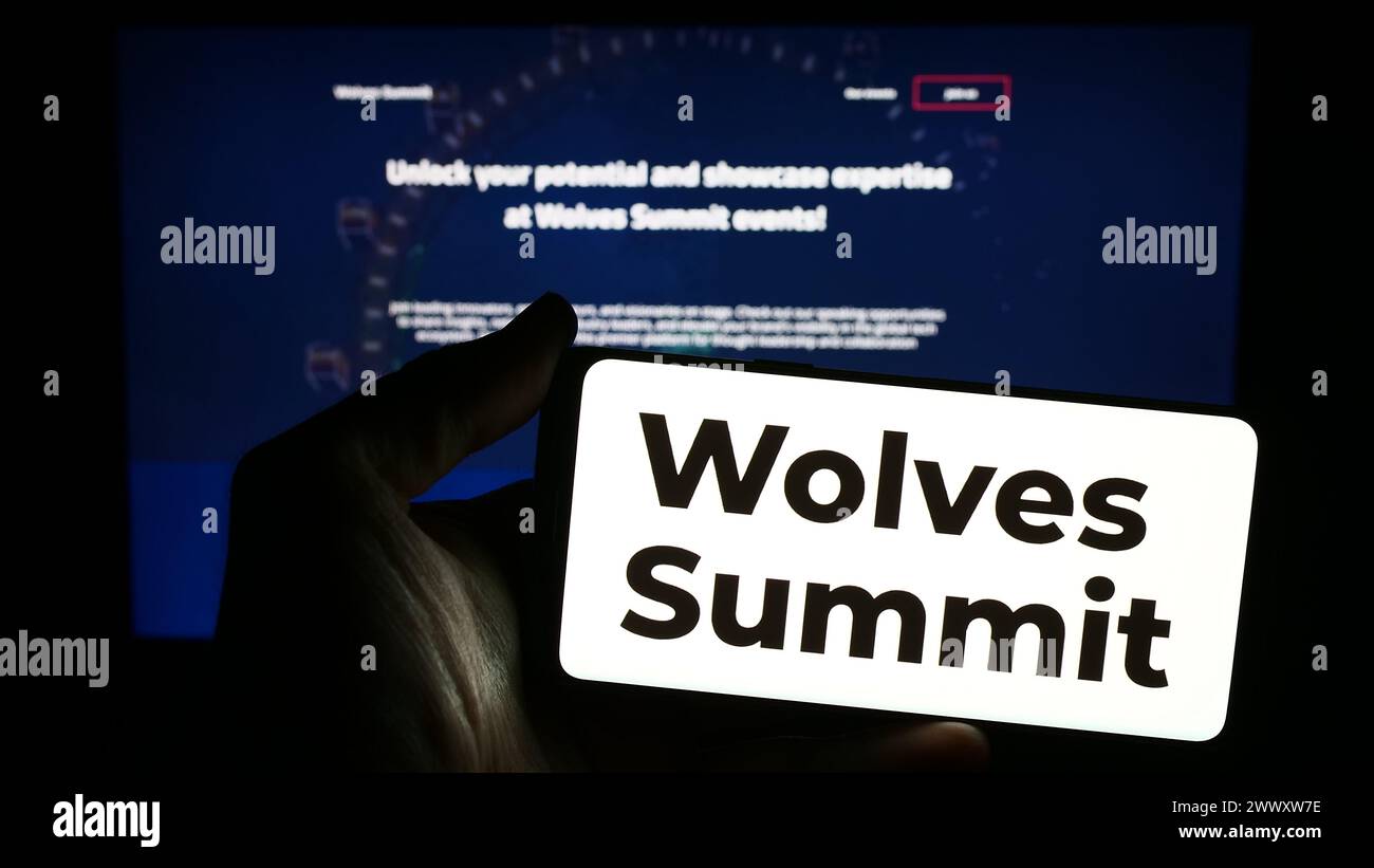 Person holding smartphone with logo of digital marketing platform Wolves Summit in front of website. Focus on phone display. Stock Photo