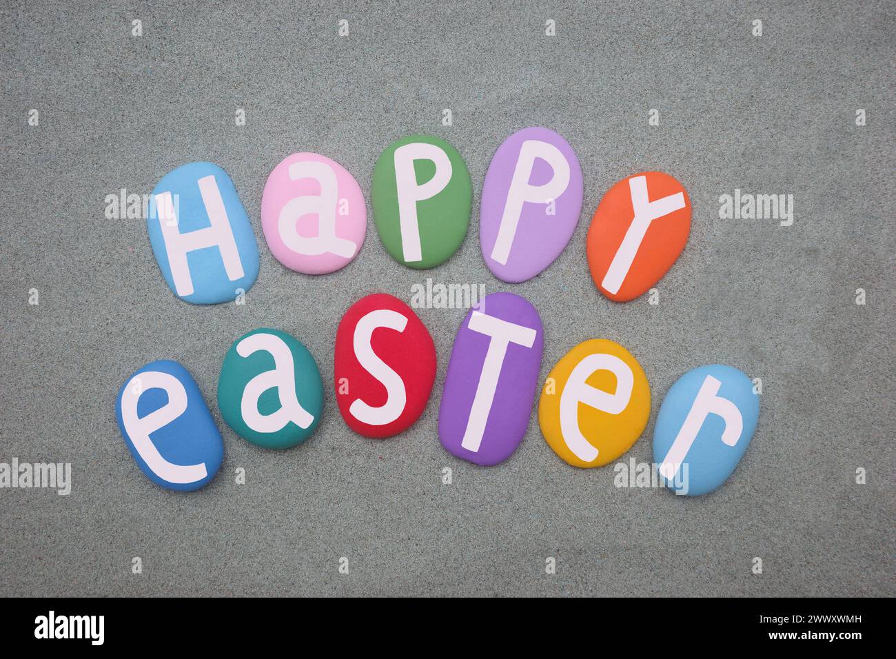 Happy Easter, creative celebration with hand painted multi colored stone letters over green sand Stock Photo