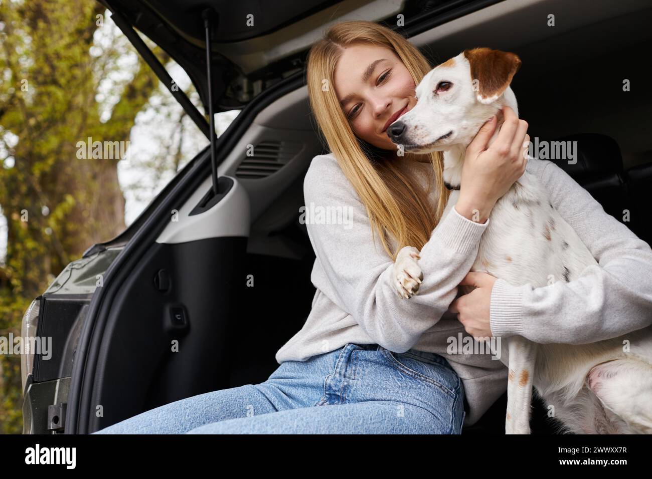 Happy girl interacting with her pet looking at dog at hiking rest halt in back of car Stock Photo