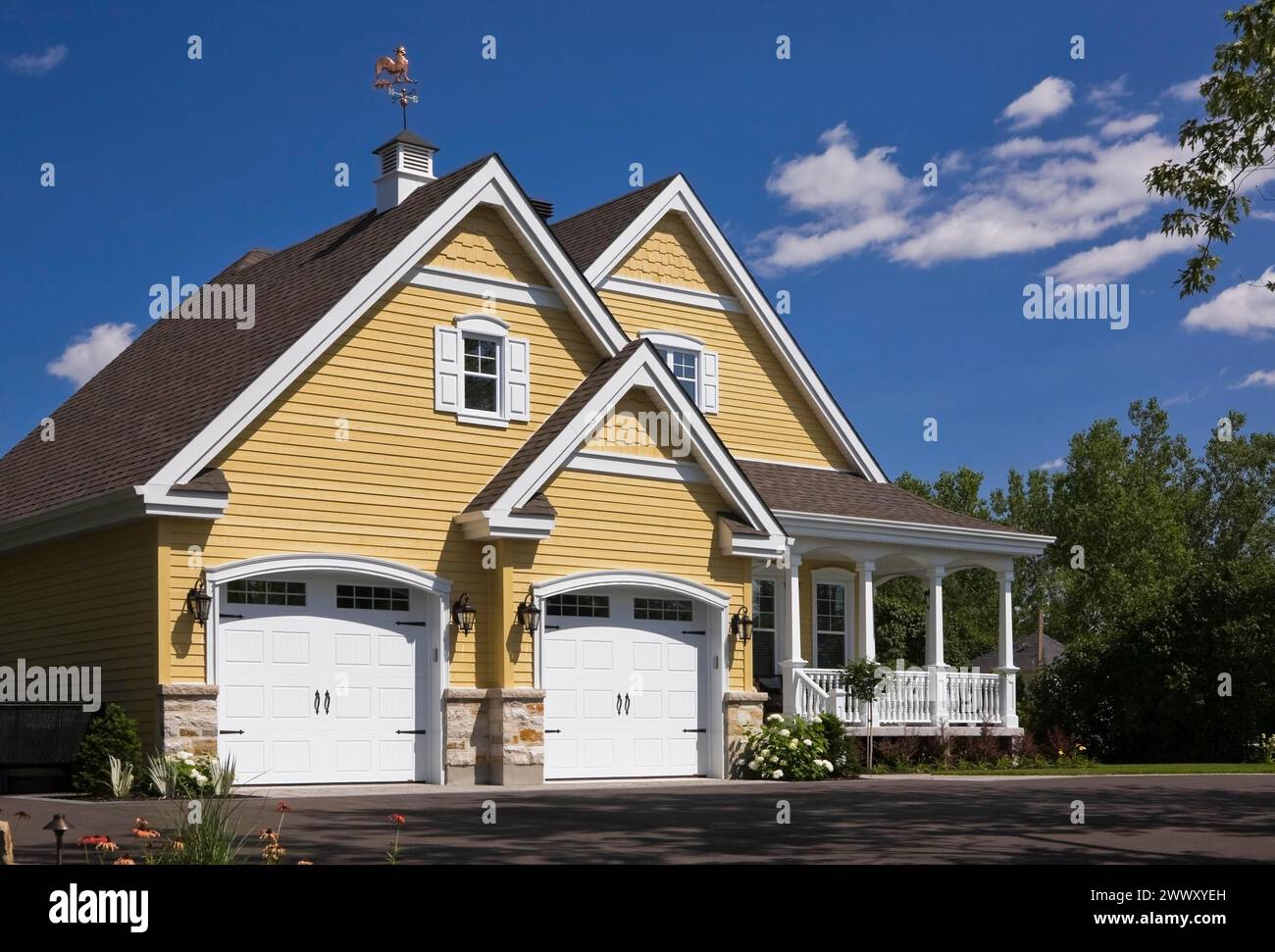 Yellow and white trim contemporary country house with two car garage, landscaped front yard and black asphalt driveway in summer, Quebec, Canada Stock Photo