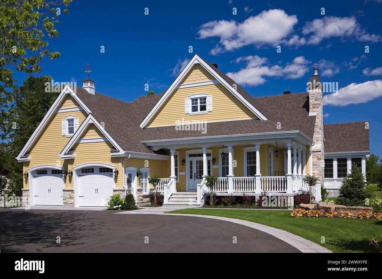 Yellow and white trim contemporary country house with two car garage, landscaped front yard and black asphalt driveway in summer, Quebec, Canada Stock Photo