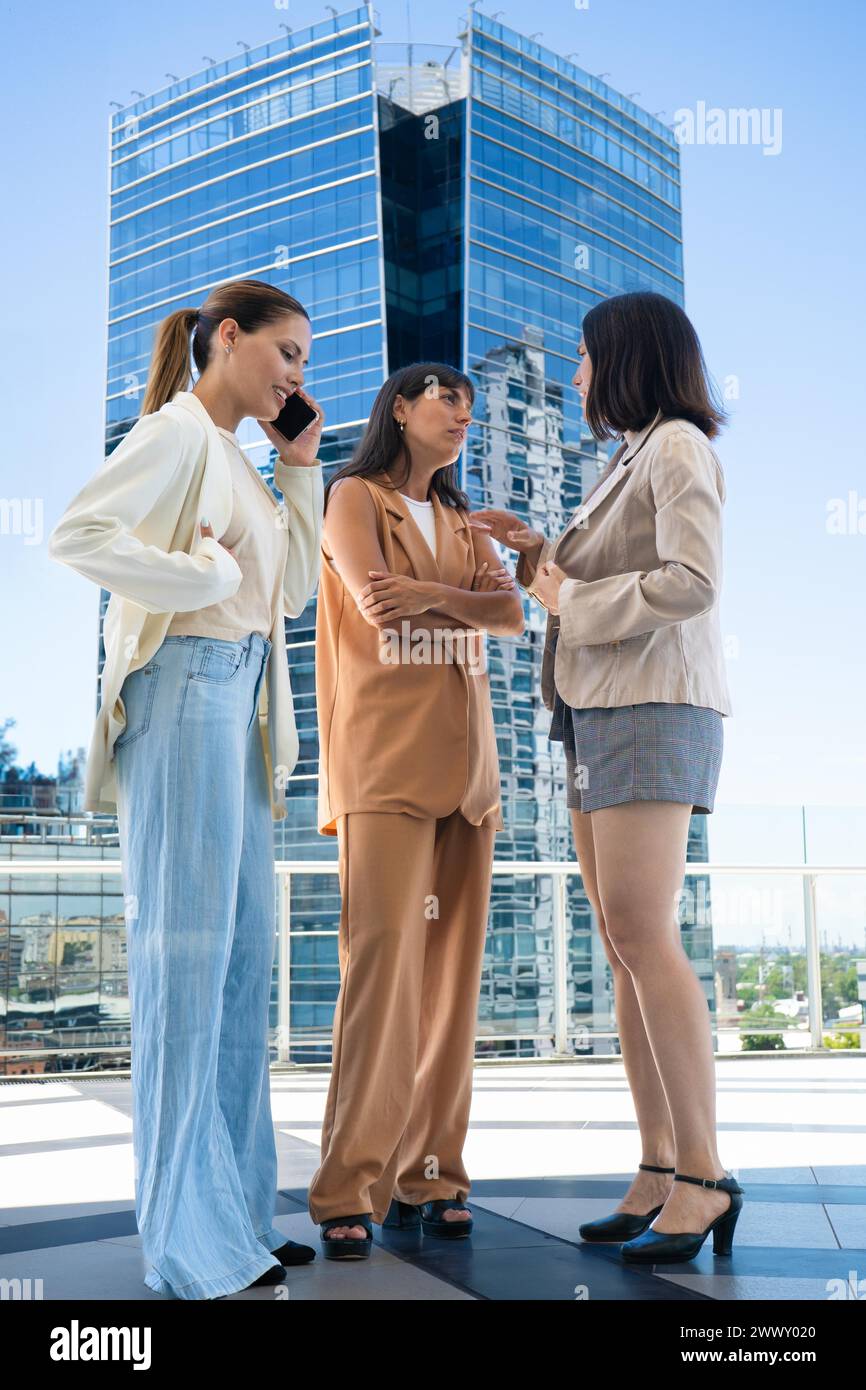 Low-angle view of three colleagues on a coffee break. One of them is talking on her cell phone while the others are chatting Stock Photo