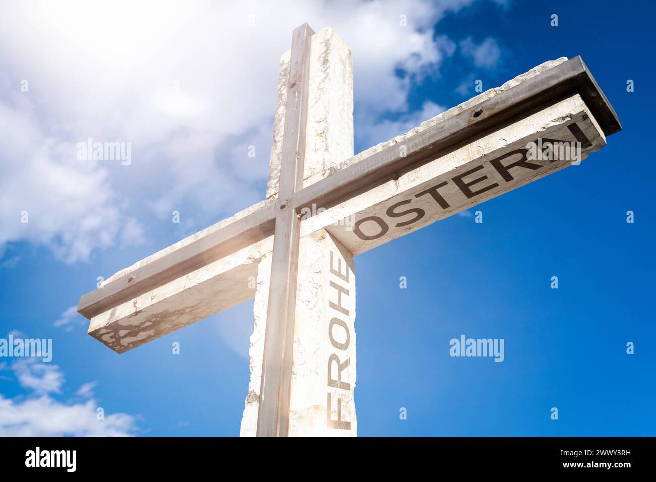 March 26, 2024: Christian cross in front of a blue sky with the inscription: Happy Easter Religion and faith concept. PHOTOMONTAGE *** Christliches Kreuz vor blauem Himmel mit der Aufschrift: Frohe Ostern Relgion und Glaube Konzept. FOTOMONTAGE Stock Photo