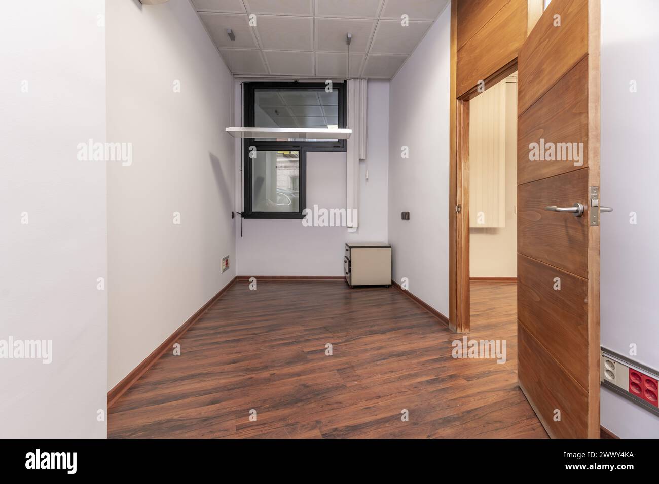 An empty office with aluminum windows, dark wooden door carpentry, reddish parquet floors and technical ceilings Stock Photo