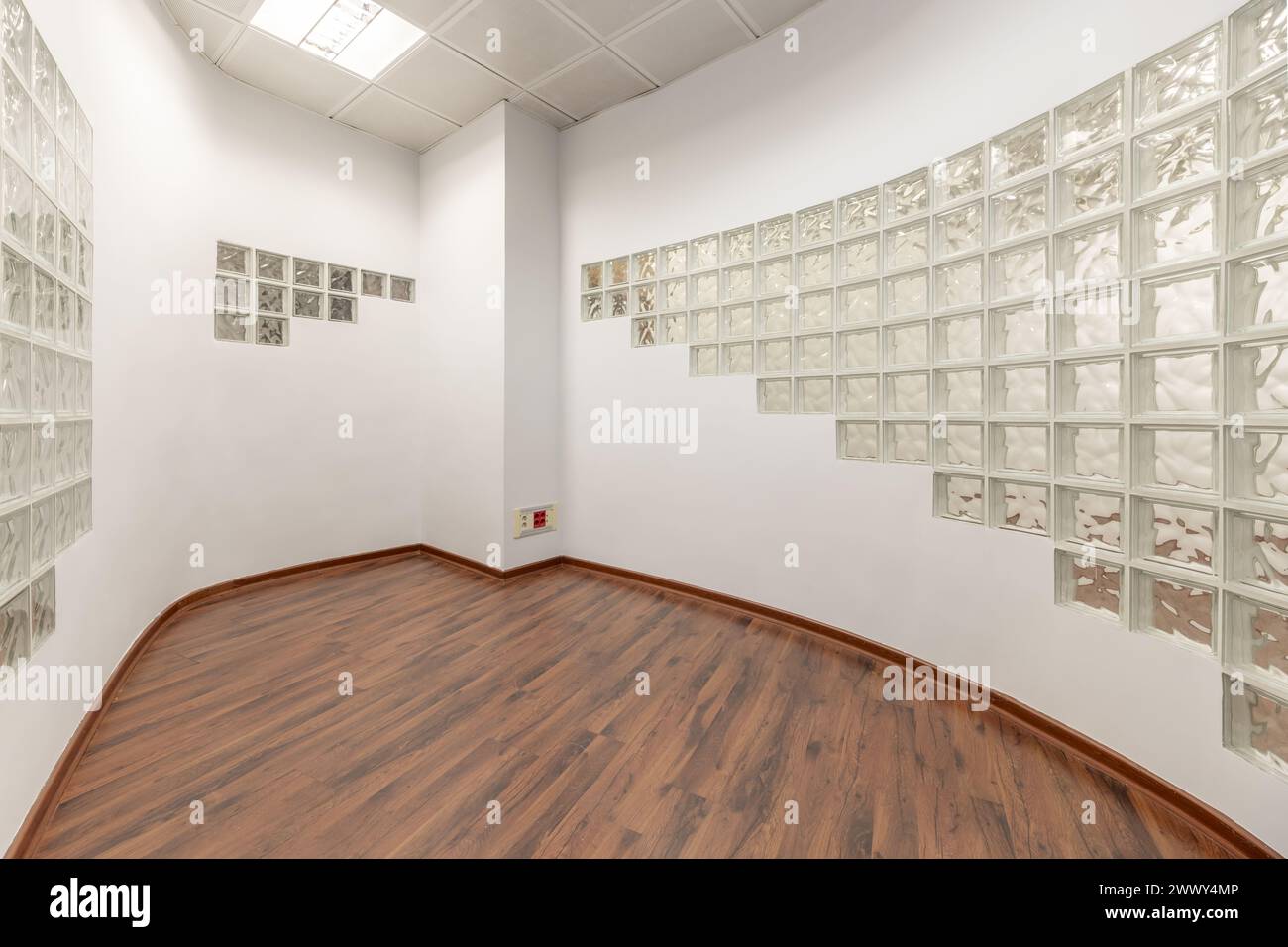 An empty office with smooth walls painted white, curved wall with glass bricks, reddish parquet floors and technical ceilings Stock Photo