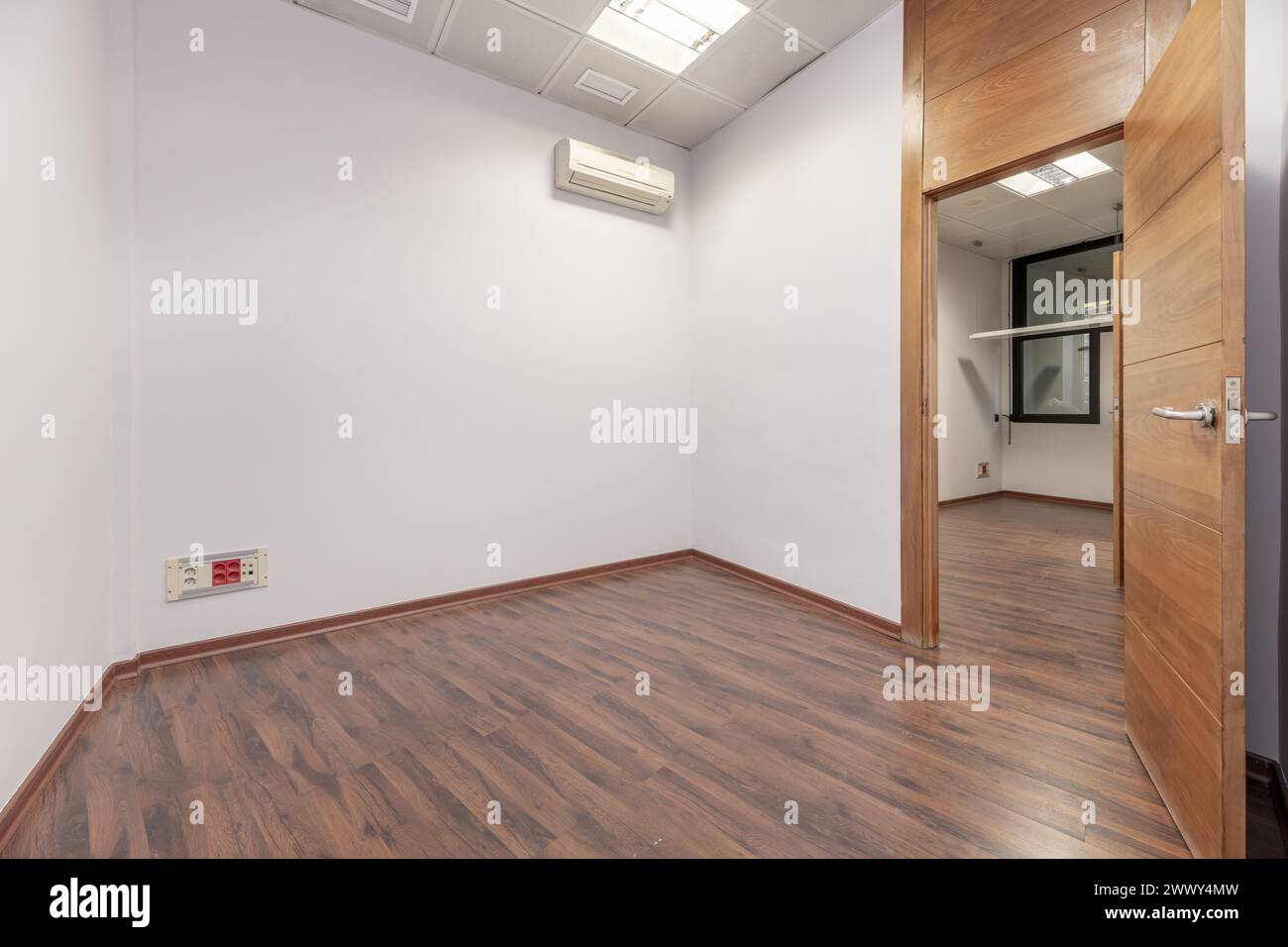 An empty office with plain white painted walls, reddish parquet floors and technical ceilings Stock Photo