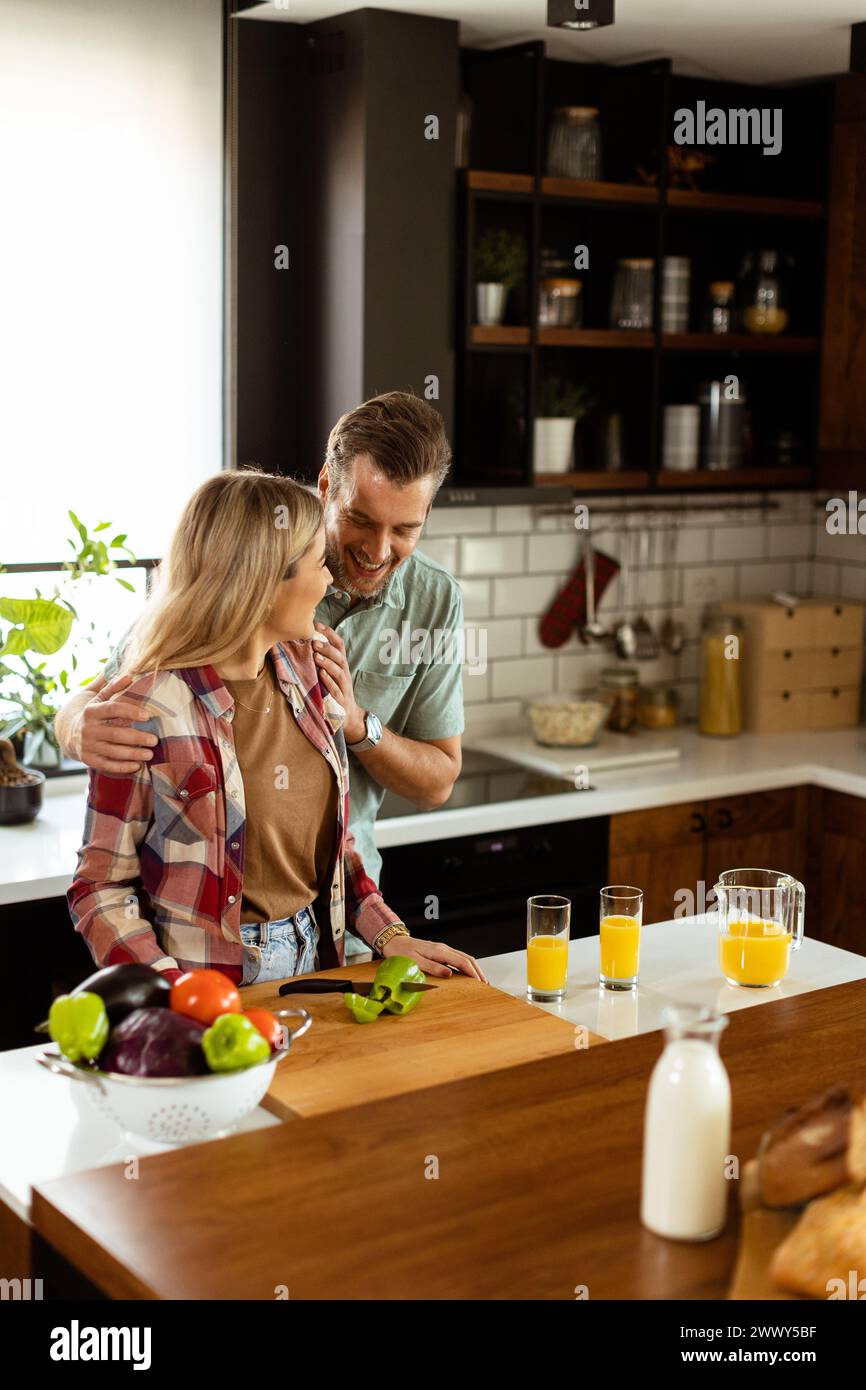 A happy couple enjoys a casual conversation with morning drinks in their sunny kitchen. Stock Photo