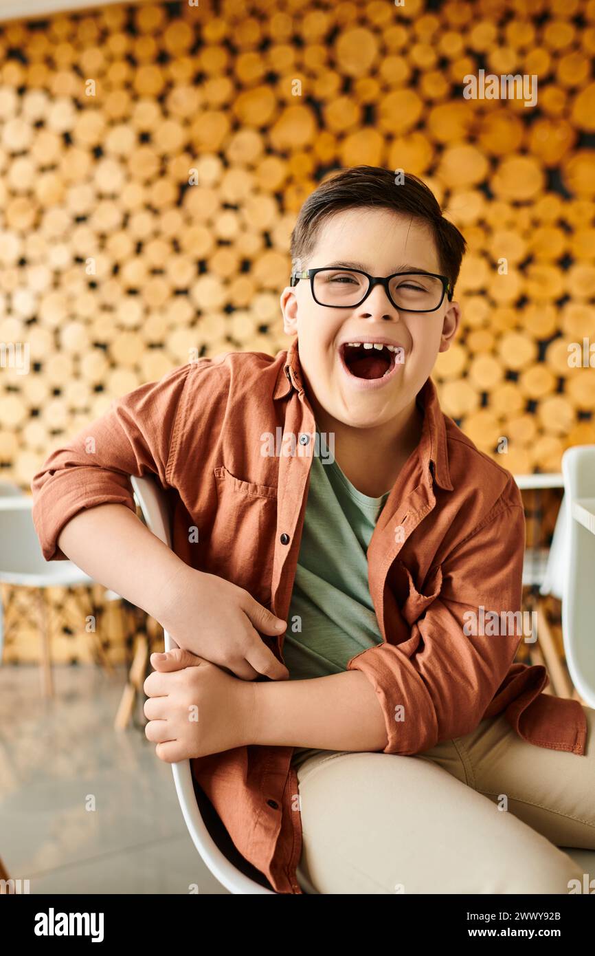happy inclusive preteen boy with Down syndrome with glasses sitting in cafe and laughing at camera Stock Photo