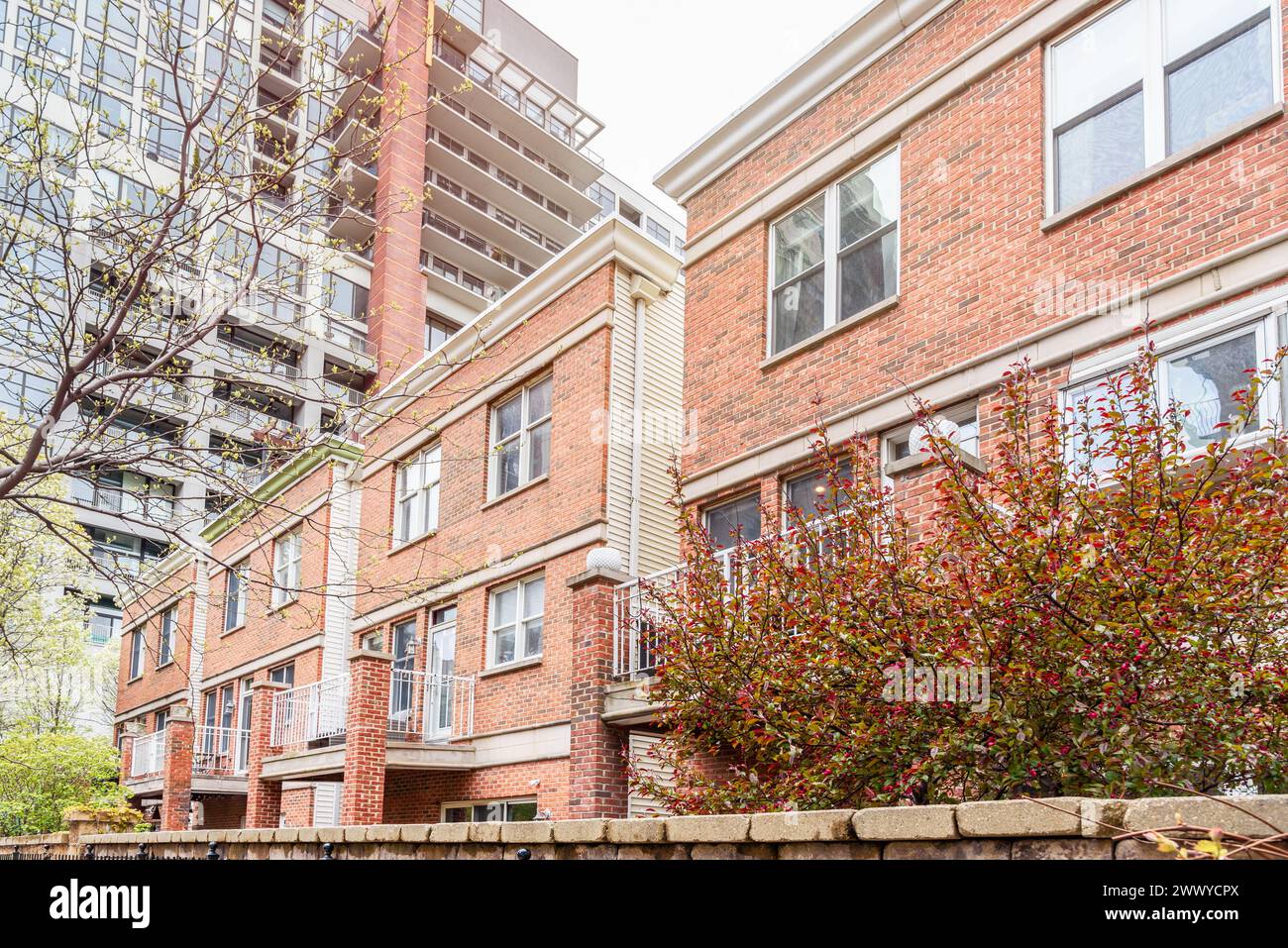 Brick row houses in a walled housing development on a cloudy spring day. A modern high rise apartment building is in background. Stock Photo