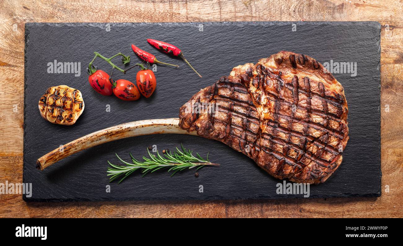 Grilled  delicious  tomahawk steak and some seasonings on black slate serving plate. Flat lay. Stock Photo