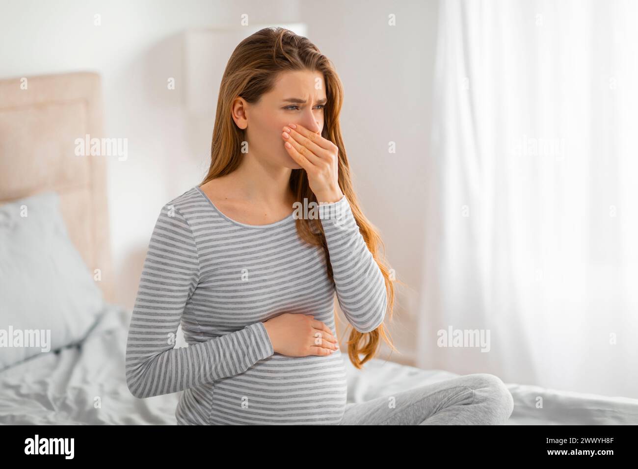 Pregnant woman feeling nauseous in bedroom Stock Photo