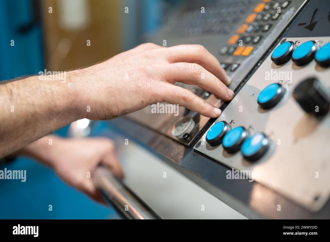 Worker pressing buttons on CNC machine control board in factory. High quality photography. Stock Photo