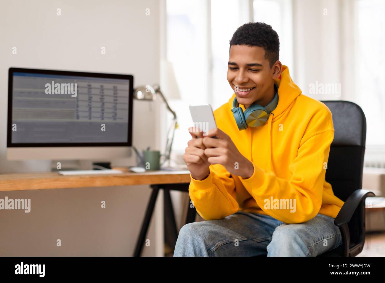 Smiling young man using smartphone at desk Stock Photo
