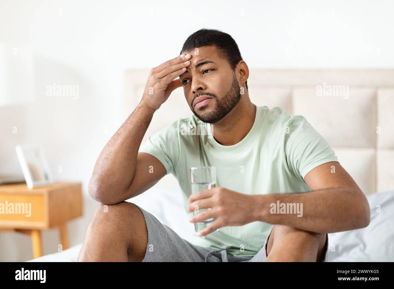 Man on bed with hand on forehead Stock Photo