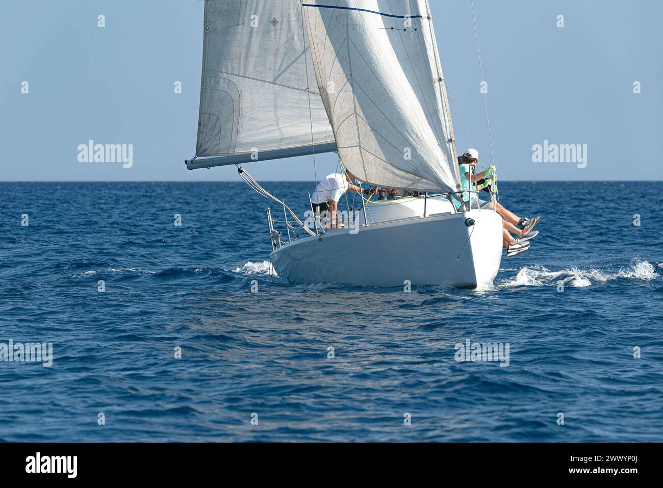 Crew navigates a sailboat on the blue ocean under clear skies Stock Photo