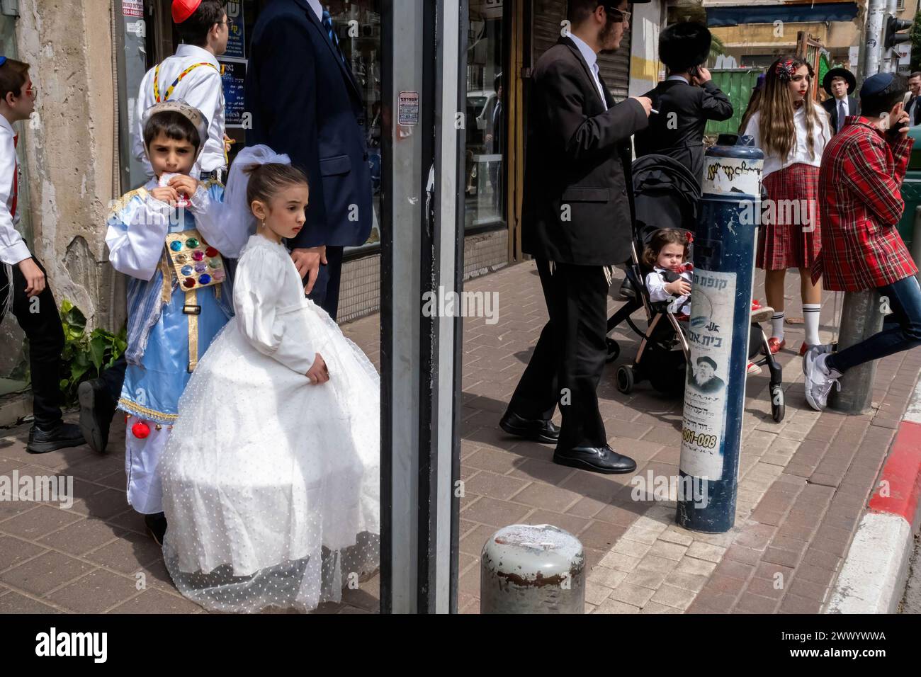 A girl is seen dressed in a white dress as Queen Esther and a boy next to her is dressed as a 'Cohen',  or high priest, according to Jewish Tradition during the Purim celebration. Ultra-Orthodox Jews Celebrate Purim in Bnei Brak, Israel. The holiday commemorates the salvation of the Jews in ancient Persia from a plot to annihilate them. A joyous holiday, it is celebrated by both secular and nonsecular Jews, most notably by dressing up in costumes and drinking, according to the Talmud, “until they cannot distinguish between ‘cursed is Haman’ and ‘blessed is Mordechai.' Stock Photo