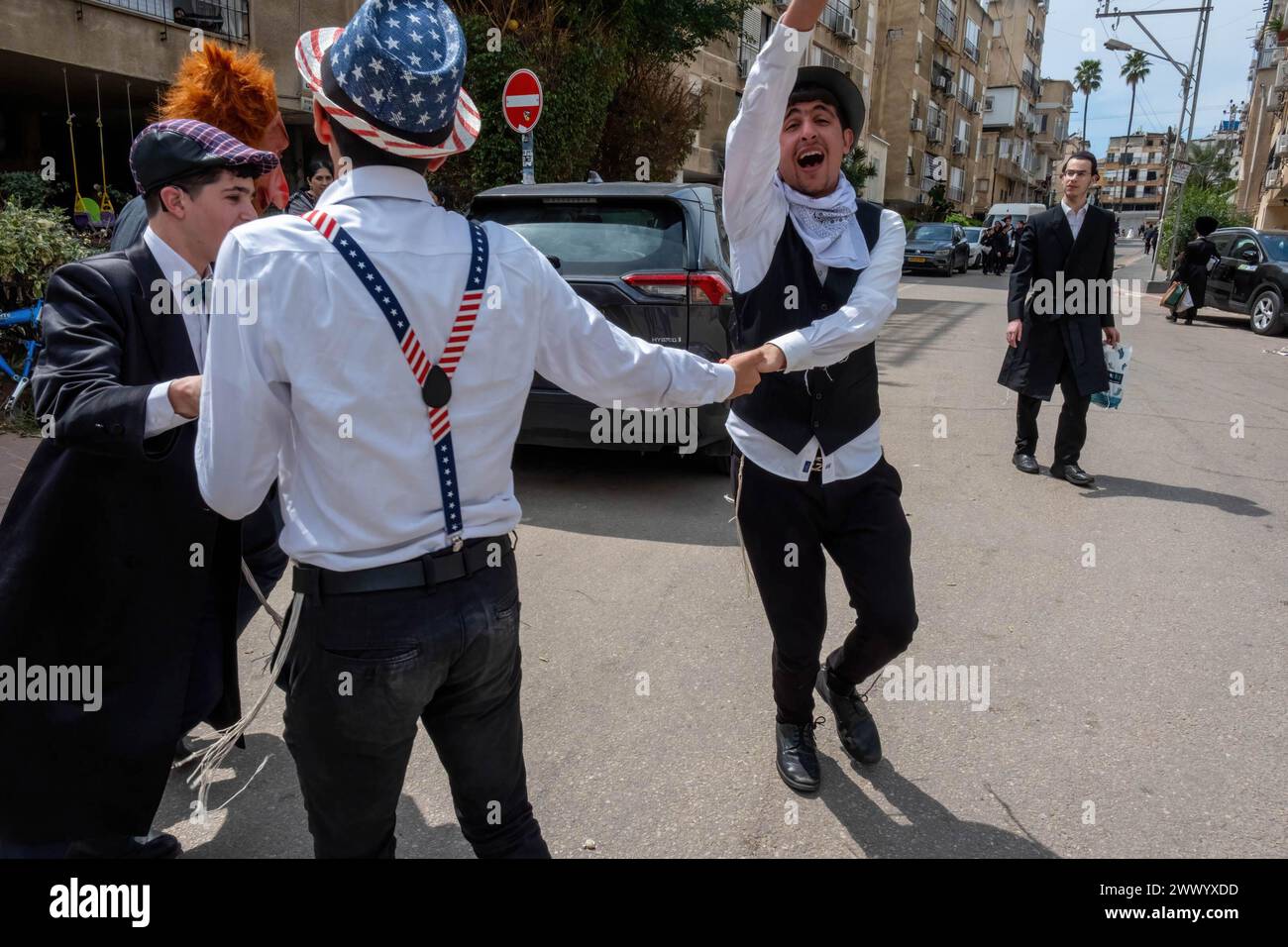 Bnei Brak, Israel. 24th Mar, 2024. Young men dressed in fancy clothing dance in the street during the Purim celebration. Ultra-Orthodox Jews Celebrate Purim in Bnei Brak, Israel. The holiday commemorates the salvation of the Jews in ancient Persia from a plot to annihilate them. A joyous holiday, it is celebrated by both secular and nonsecular Jews, most notably by dressing up in costumes and drinking, according to the Talmud, “until they cannot distinguish between ‘cursed is Haman' and ‘blessed is Mordechai.' (Photo by Syndi Pilar/SOPA Images/Sipa USA) Credit: Sipa USA/Alamy Live News Stock Photo