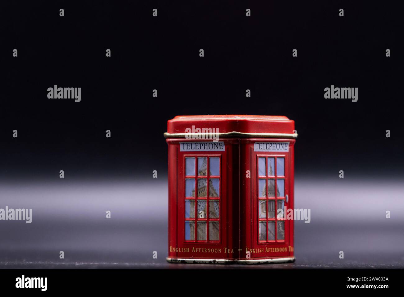 Echoes of time. Red, dusty miniature souvenir telephone booth with letters English afternoon tea and abstract fog in the black background. Stock Photo