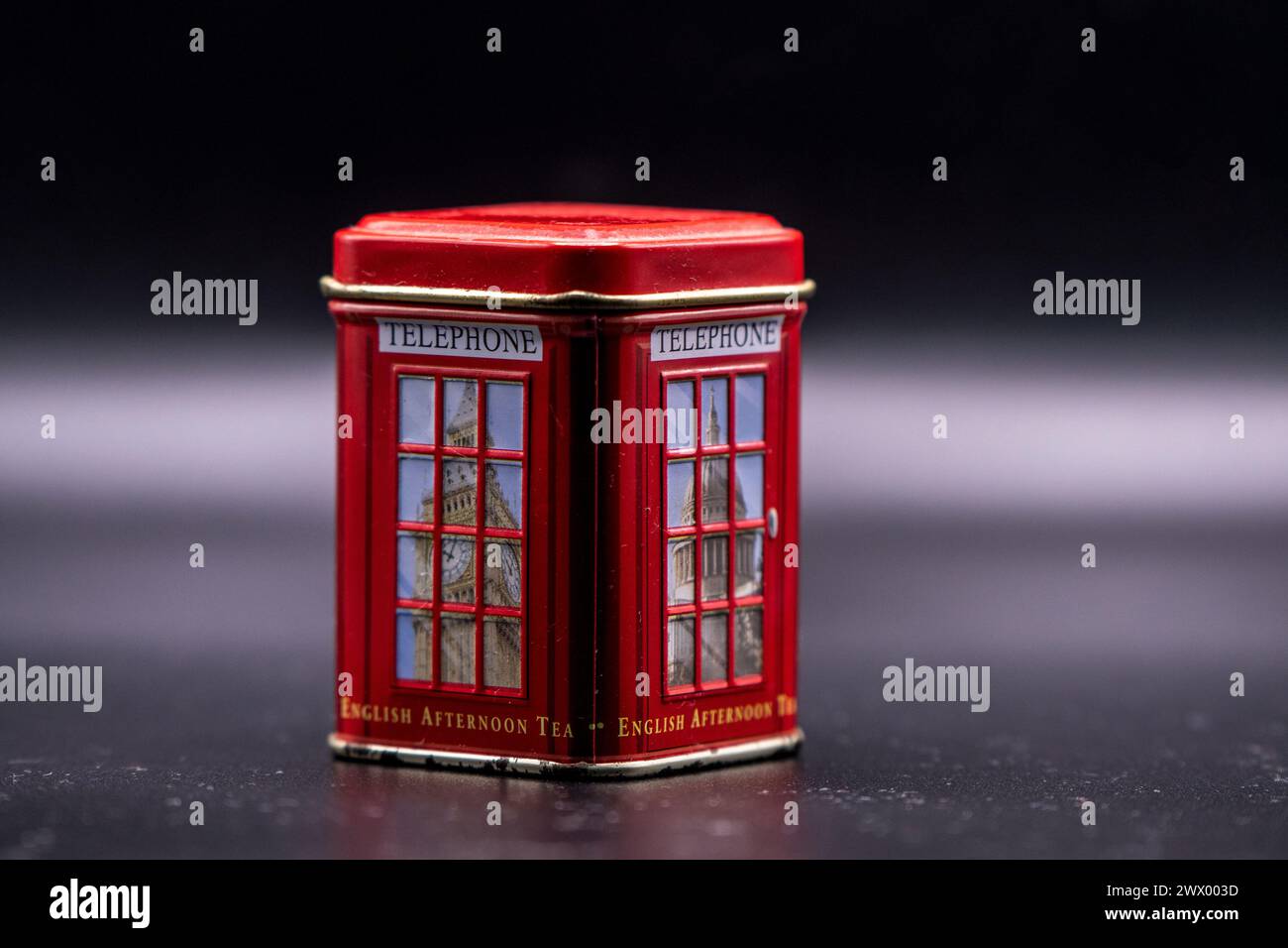 Echoes of time. Red, dusty miniature souvenir telephone booth with letters English afternoon tea and abstract fog in the black background. Stock Photo