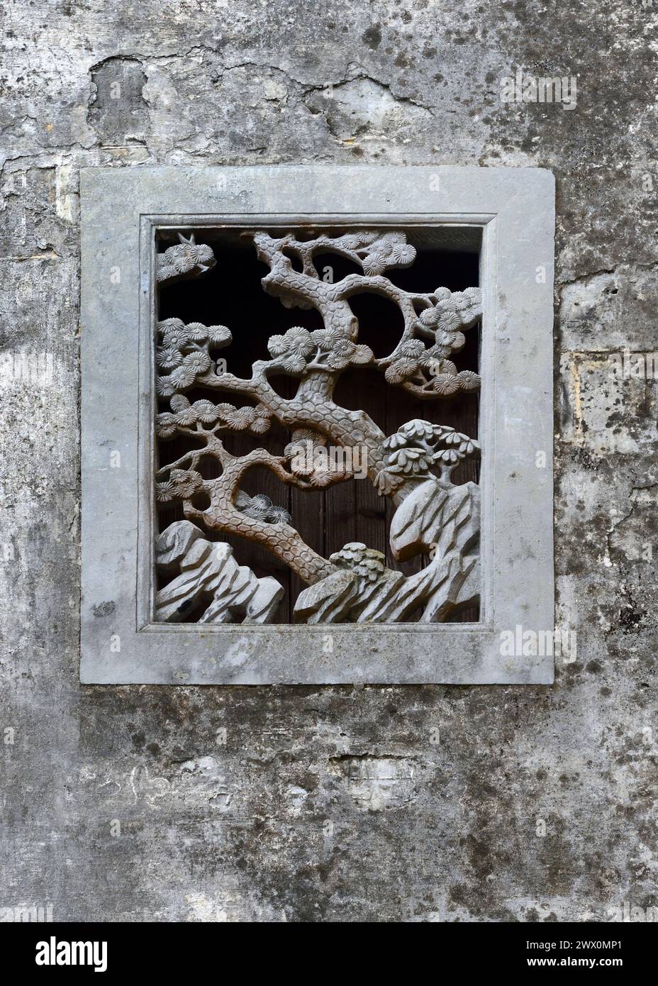 A stone carving cut-out creates a small, decorative window in a rock wall in Xidi Ancient Town. Stock Photo