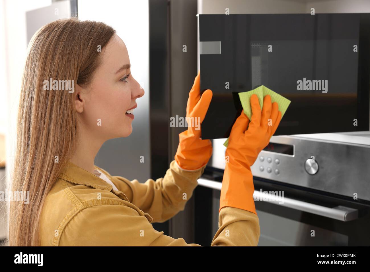 Woman with microfiber cloth cleaning microwave in kitchen Stock Photo