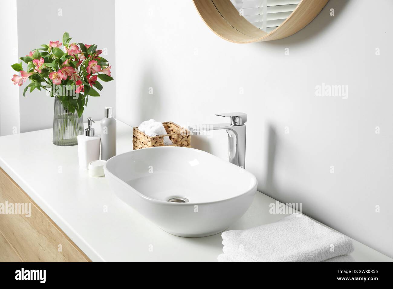 Vase with beautiful Alstroemeria flowers and toiletries near sink in bathroom Stock Photo