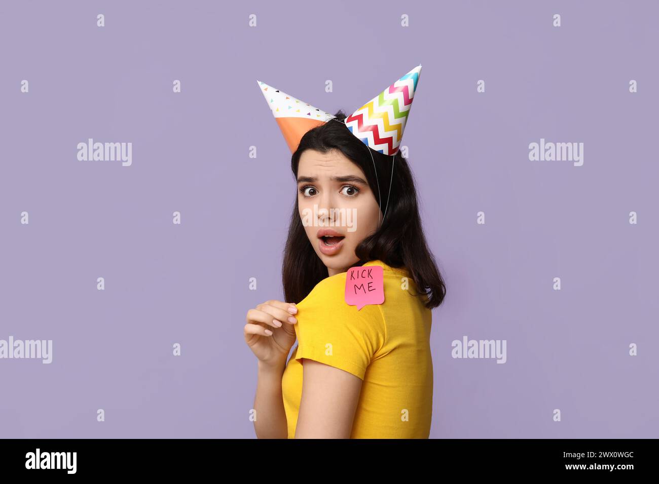 Beautiful young shocked woman with paper sticker attached to her back on purple background. April fool's day celebration Stock Photo