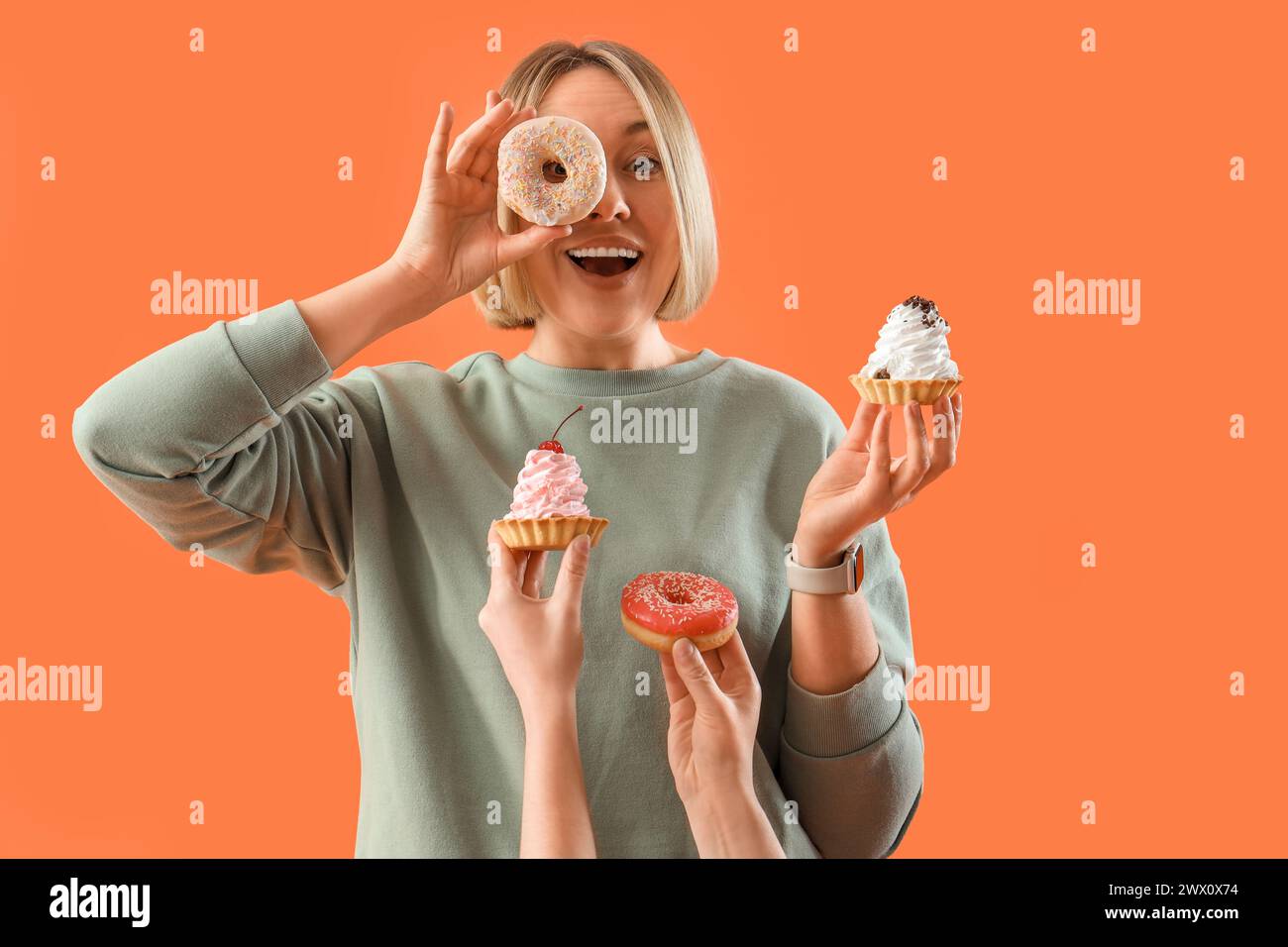 Beautiful woman and hands with treats on orange background. Overeating concept Stock Photo