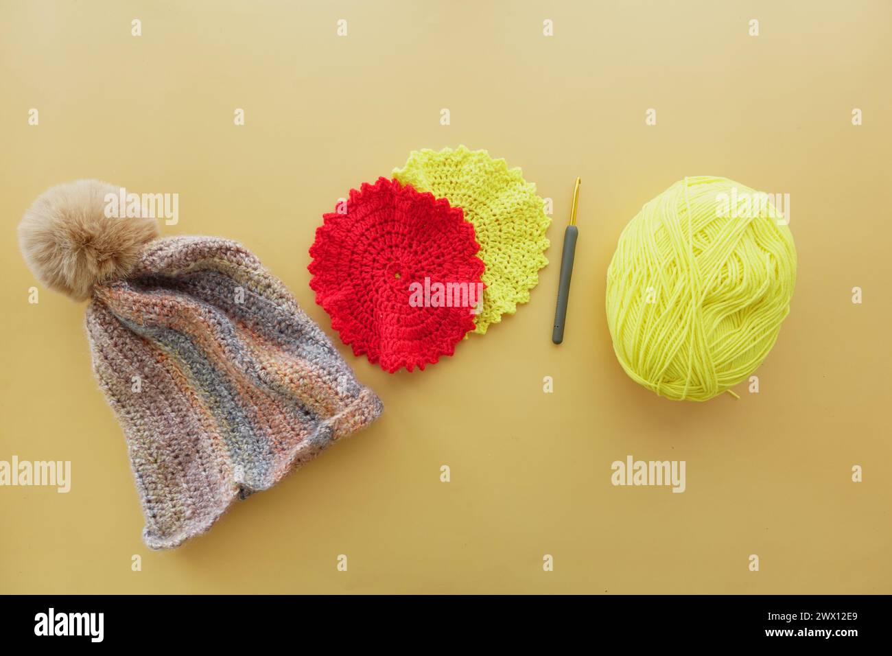 A magenta crocheted cap with woolen yarn and crochet hook displayed on table Stock Photo